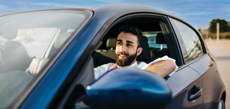 Man in driver's seat with the window down and his arm resting on the door frame