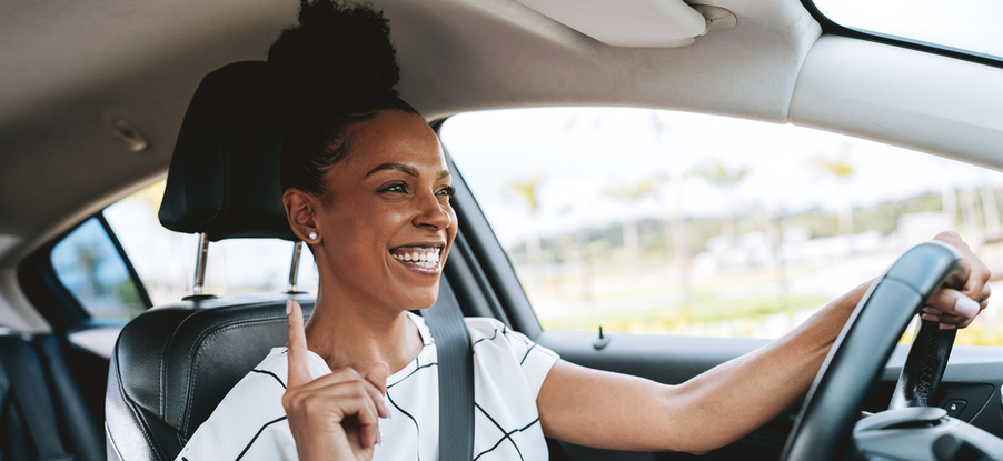 A woman driving in her car singing and smiling.