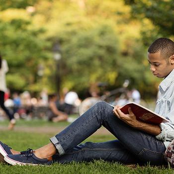 Young man reading under tree.