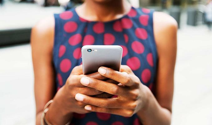 Close up of woman in a blue dress with red polka dots using a phone.