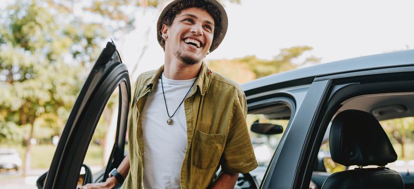 A young smiling man is getting out of his car.