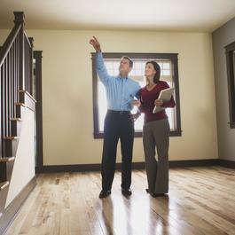 Man and woman in empty house inspecting something near the stairs.