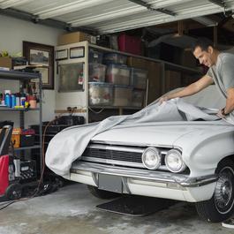 Man in jeans putting cover over a white classic car.