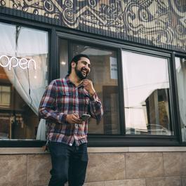 A smiling man standing in front of a restaurant while holding his smartphone