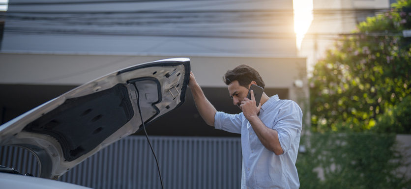 Man looking under the hood of a car while speaking on the phone 