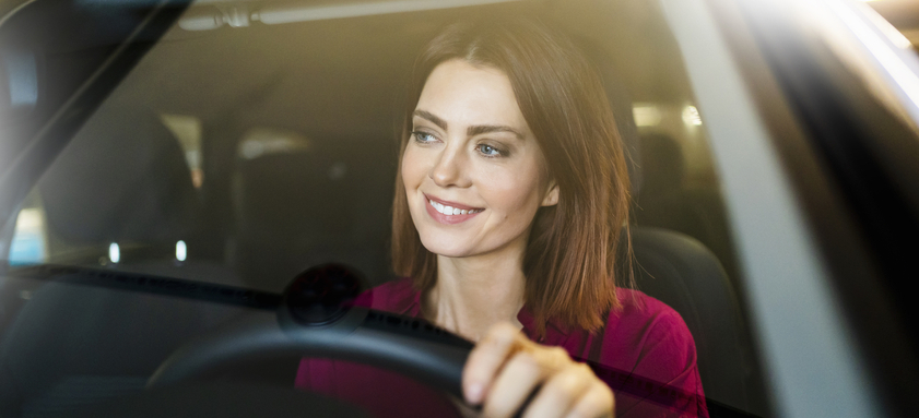 Happy businesswoman driving car seen through windshield.