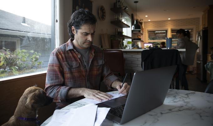 man working on laptop at kitchen table with dog