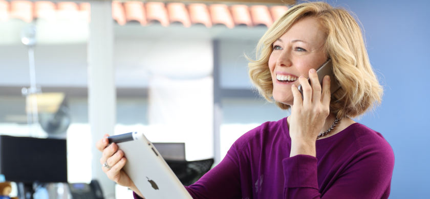Woman on the phone smiling while holding a tablet.
