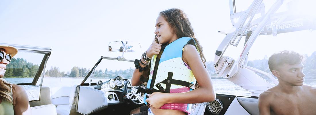 Young girl putting on life vest before going swimming while out on boat.