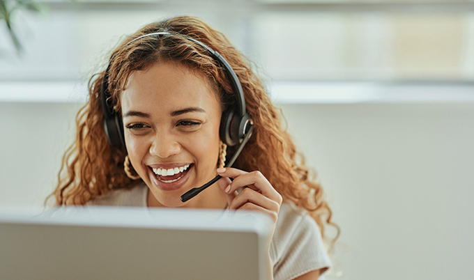 Customer service agent smiling in front of a computer on her headset.