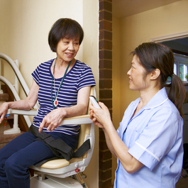 Caregiver helping a woman up a stair lift chair.
