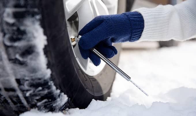 Gloved hand checking tire pressure on a tire in snow.