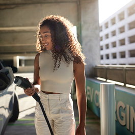 Young woman holding electric plug by car at charging station