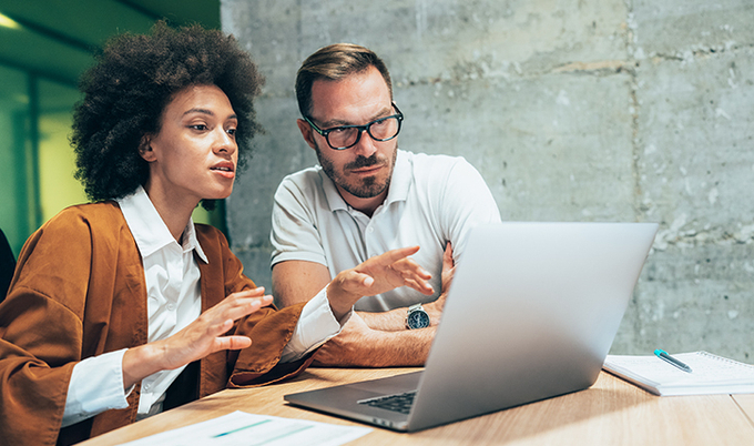 Two co-workers reviewing something on a laptop.