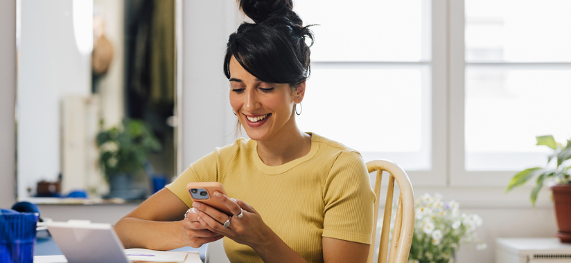 woman with dark hair sitting on chair looking at mobile phone in her hand