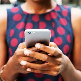 Close up of woman in a blue dress with red polka dots using a phone.