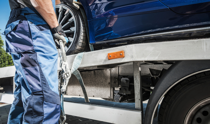 Male Worker Putting Transport Belts Around the Wheel of a Car on His Trailer to Secure It for Safe Carriage. Vehicle Transportation Theme.