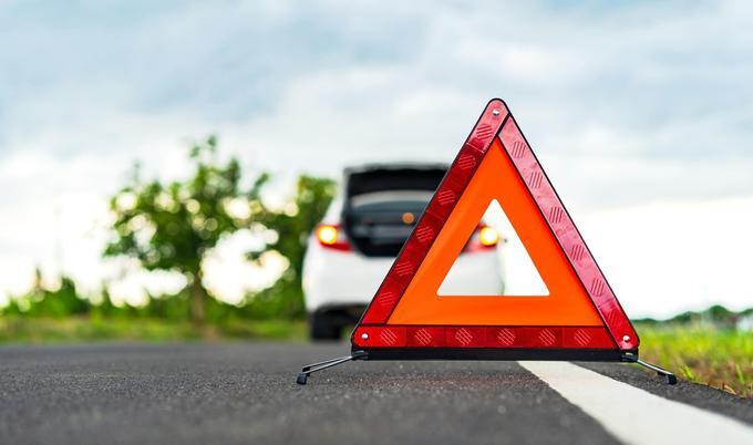 white car parked on side of the road with a reflector triangle out behind it.