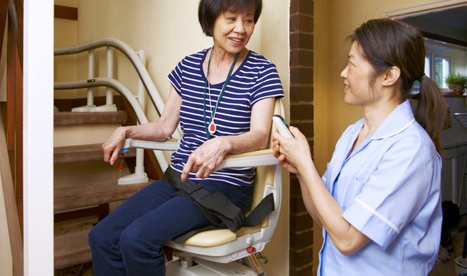 Caregiver helping a woman up a stair lift chair.