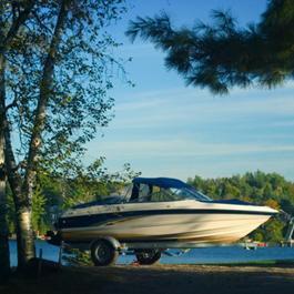 Boat on tow hitch on a dirt road in front of a lake.