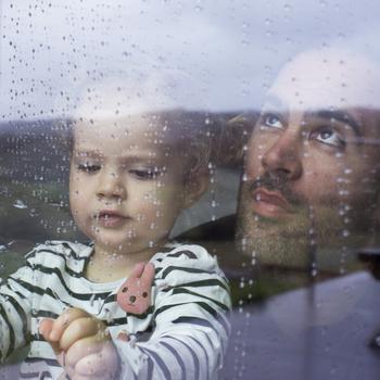 Man and little girl looking at raindrops through a window.