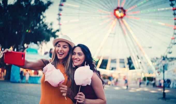 Women at the amusement park eating pink cotton candy.