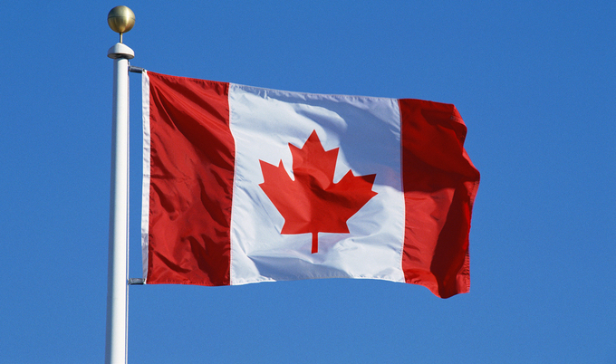 A closeup of the Canadian flag on a flagpole, waving in the wind with a clear blue sky in the background.