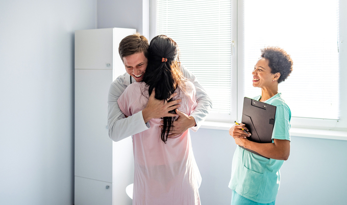 Young male doctor hugging patient while female nurse smiles