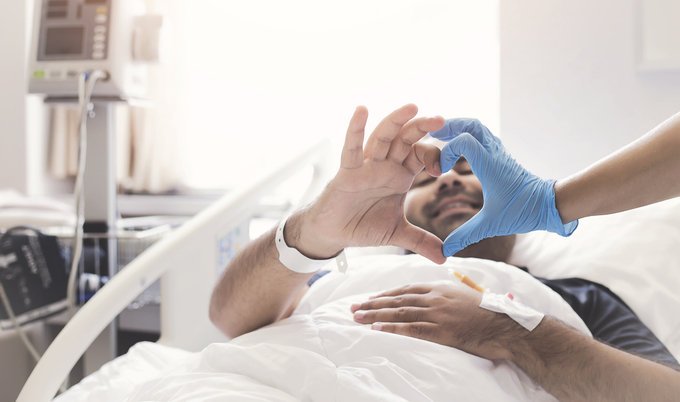 Man in hospital bed holding hand up to make heart shape with nurses hand
