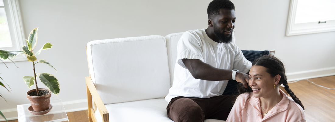 man braiding girlfriends hair in living room