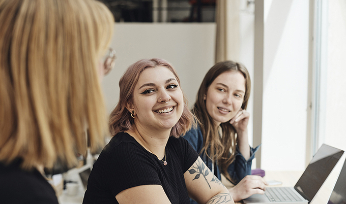 Two women sitting at their computers having a discussion in an office.