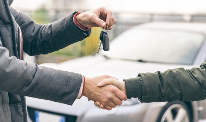 Two people shaking hands and handing over car keys.