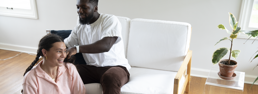 man braiding girlfriends hair in living room