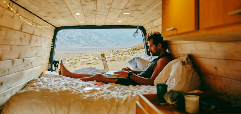 Young man on bed with laptop in camper van