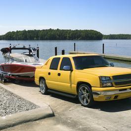 Yellow pickup truck backing red power boat on trailer into lake. 