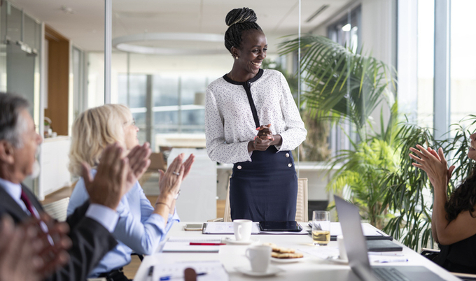Woman speaking at the head of a table in a conference room.