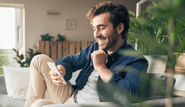 Man sitting on couch at home, using smartphone
