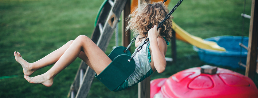 Little girl with crazy curly hair and swimsuit swings on a backyard swing set.