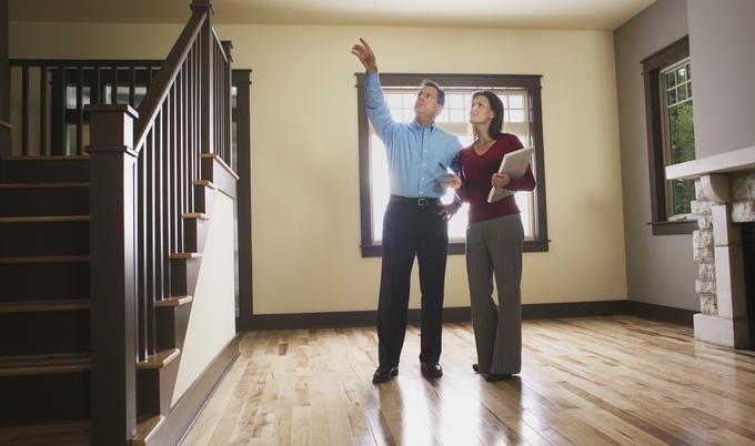 Man and woman in empty house inspecting something near the stairs.