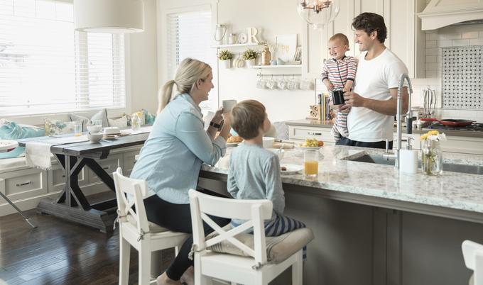 A family is eating breakfast and smiling while sitting in the kitchen.