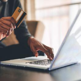 Person sitting down holding a credit card in one hand while other hand is on a laptop. 