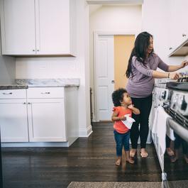 Mom working in kitchen with child standing near her.