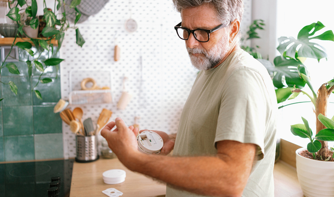 A person in a modern kitchen closely examines or installs a small round smoke detector device.