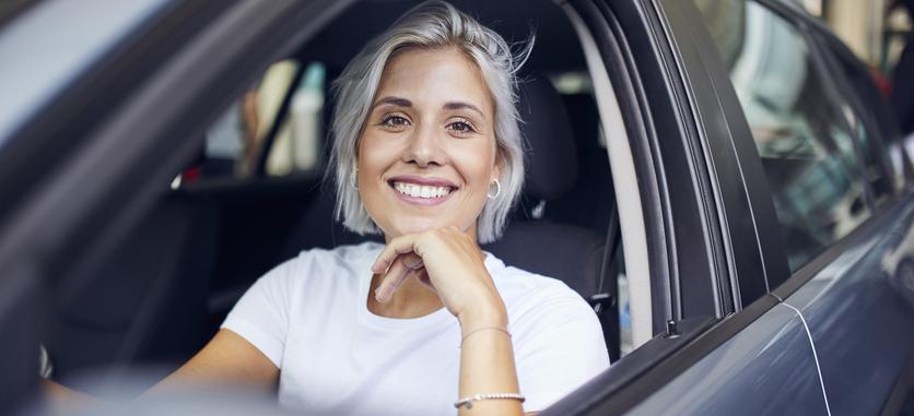 A woman sitting in the driver's seat, smiling with gray hair.
